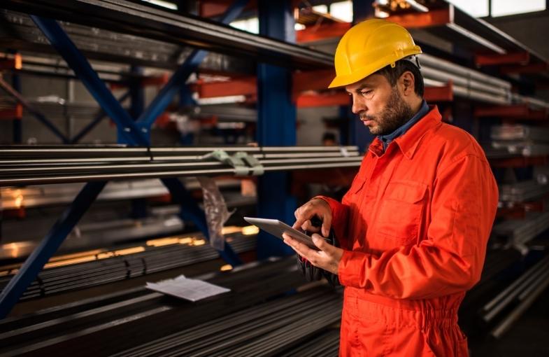 Trabajador industrial utilizando una tablet para realizar mantenimiento predictivo en una fábrica. La imagen representa el uso de tecnologías como sensores y análisis de datos para optimizar procesos y reducir costes, clave en la Industria 4.0.